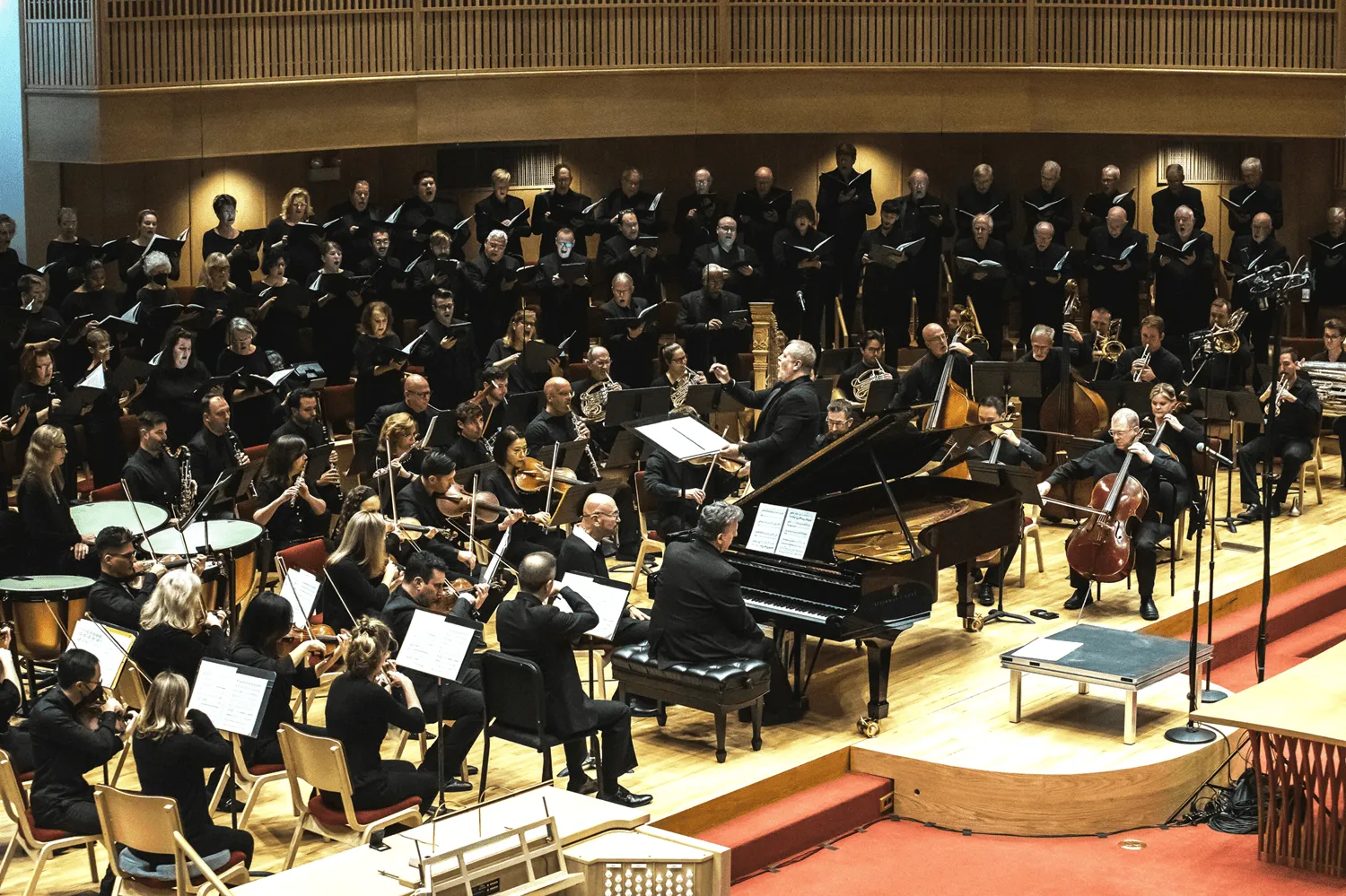 Key Chorale performing with a full symphony orchestra on stage, led by a conductor with choir and musicians in concert.